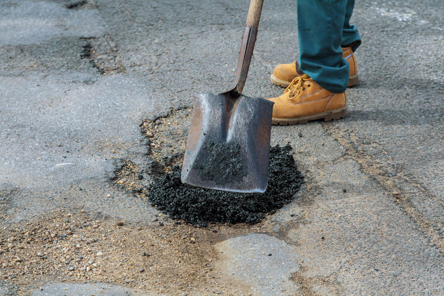 Road crew member filling a pothole wit blacktop.